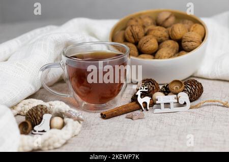 Cup of tea and nuts, cones, cinnamon sticks, small sled and deer, white cloth. Christmas, winter concept. Side view lay flat. Stock Photo