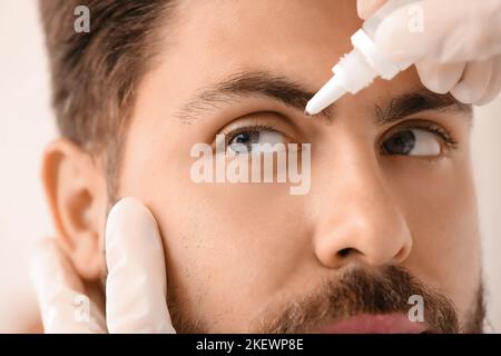 Ophthalmologist putting drops in young man's eye at hospital, closeup Stock Photo
