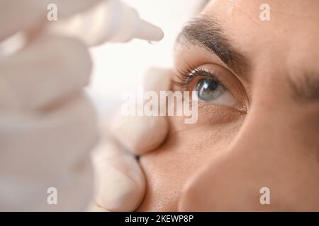 Ophthalmologist putting drops in young man's eye at hospital, closeup Stock Photo