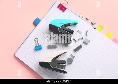 Open notebook, staplers and staples on pink background Stock Photo