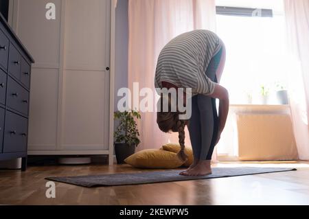 Mature woman doing stretching at home. Uttanasana yoga pose Stock Photo