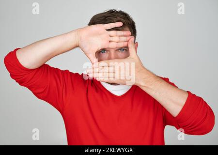 young man covering his face by hand and looking at camera peeking Stock Photo