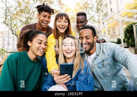 Young happy friends having fun together using mobile phone sitting outdoors Stock Photo