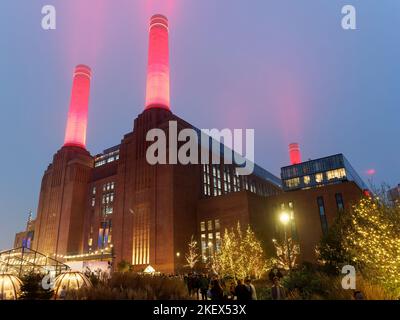 View looking up at Battersea Power Station in London illuminated at night with bright red chimneys piercing the sky Stock Photo