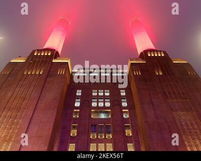 View looking up at Battersea Power Station in London illuminated on a misty night with bright red chimneys piercing the sky Stock Photo