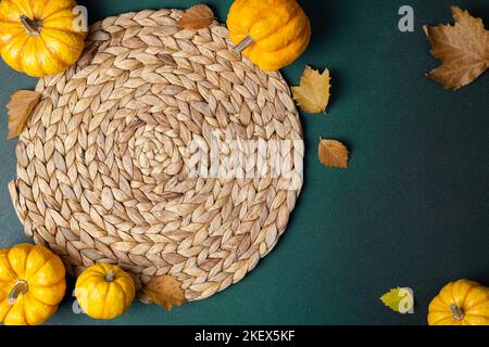 Autumn cozy table setting background. Top view of wicker place mat, pumpkins, autumn leaves on dark table. Autumnal hygge table setting. Restaurant me Stock Photo