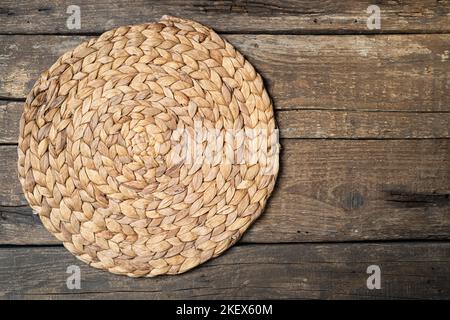 Wicker straw place mat on wooden dark background. Round woven straw mat on wooden gray dining table. Menu, dining, eating concept. Top view, copy spac Stock Photo