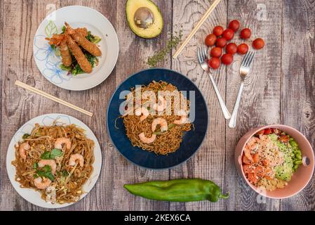 Typical Japanese food recipes with various types of sautéed noodles with seafood, tempura prawns and a poke bowl of salmon and edamame beans Stock Photo