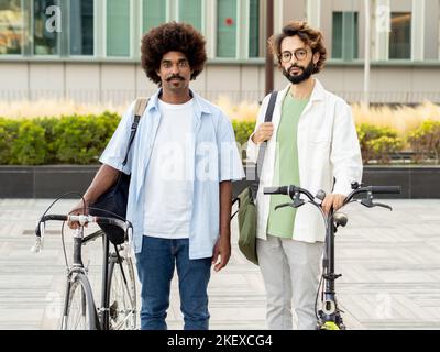 Two young diverse male entrepreneurs looking at camera serious with urban bikes in a city. Sustainable business and mobility concept Stock Photo