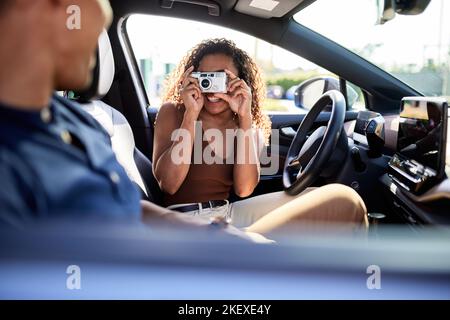 Smiling woman photographing boyfriend through camera during road trip Stock Photo