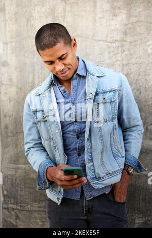Man using smart phone standing against wall Stock Photo
