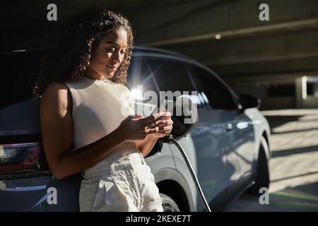Woman using smart phone by electric car at parking garage Stock Photo