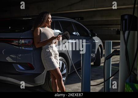 Contemplative woman with smart phone leaning on electric car Stock ...
