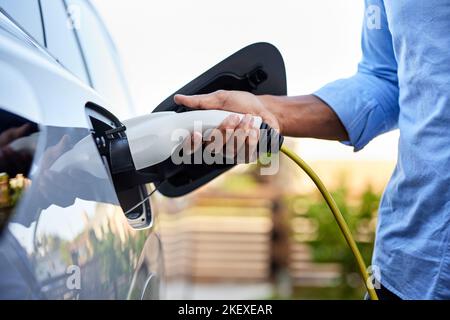 Midsection of man plugging in cable while charging electric car Stock Photo