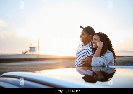 Smiling heterosexual couple by electric car enjoying sunset together Stock Photo
