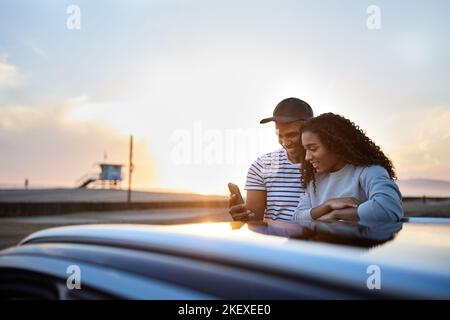 Smiling heterosexual couple using smart phone by car during sunset Stock Photo