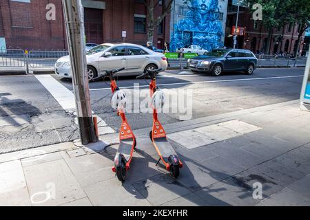 Neuron orange e electric scooters with helmets for hire on a pavement in Melbourne city centre,Victoria,Australia 2022 Stock Photo