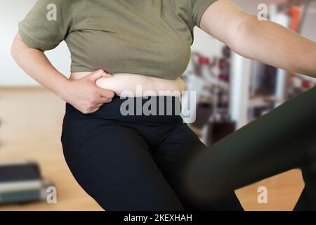 Shot of a young woman exercising at the gym on a stationary bike and pinching her fats Stock Photo