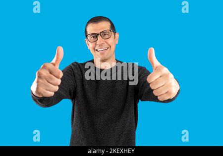 Studio shot of a man wearing casual sweater and glasses over blue background success sign doing positive gesture with hand, thumbs up smiling and happ Stock Photo