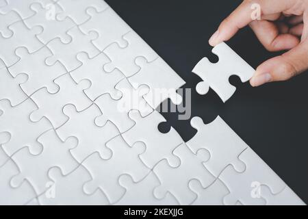 Woman assembling a jigsaw puzzle she is adding the last missing piece, solutions and challenges concept,  Hand put the last piece of jigsaw puzzle to Stock Photo