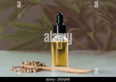 CBD oil extracted from marijuana in a glass bottle with a dropper lid, pile of hemp seeds on a wooden spoon against a background of green plants Stock Photo