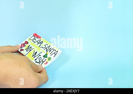 Christmas letter to Santa Claus from kid concept. Closeup of human hand holding a Dear Santa written letter drawing on white paper. Stock Photo