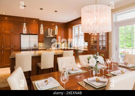 Dark stained oak wood table with white high-back leather and wood chairs, stained cherrywood island with granite countertop in dining and kitchen room. Stock Photo