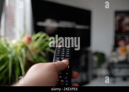 A man is holding a TV remote while selecting a program on the flat screen TV in the livingroom Stock Photo