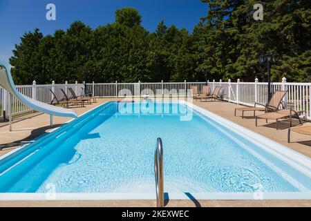 In-ground swimming pool surrounded by a white metal fence in residential backyard summer. Stock Photo