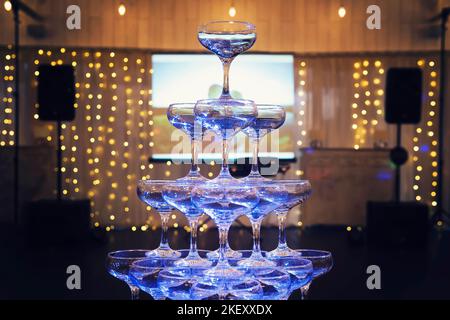 Front view short of 4-tiers champagne tower with projection screen and illuminated banquet stage background. A champagne wedding tower built in the ce Stock Photo