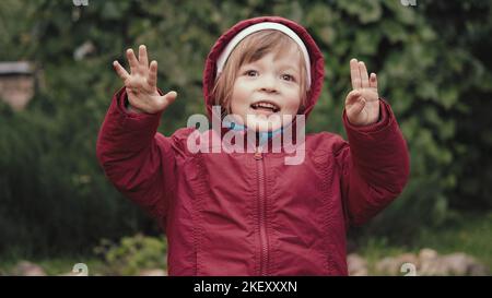 Cute little girl in a hooded jacket is happy and makes faces in front of camera Stock Photo