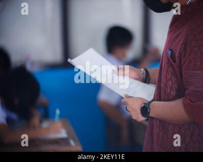 Teacher controls the exam room for students to take the exam in the classroom with wearing facemask for protection covid-19 Stock Photo