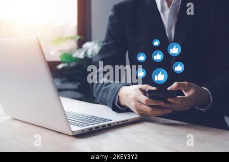 Chat and notification on smartphone, notebook (Laptop) with virtual blue like emoji social media icon. Businessman using smartphone on vacation with h Stock Photo