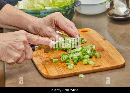 Chef cuts leek on wooden board in the kitchen Stock Photo