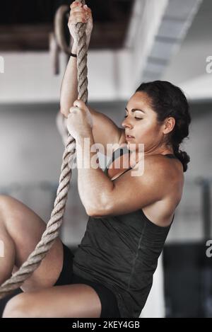 Its all about technique. a young woman climbing a rope at the gym. Stock Photo