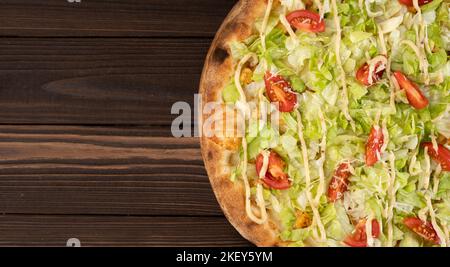 Delicious pizza Caesar with white chicken, sauce, parmesan, cherry tomatoes and fresh lettuce at wooden background. Restaurant pizzeria menu. Banner. Stock Photo