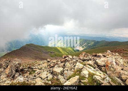 The clouds hung low over rocky slopes in the central asian mountains. Amazing view from peak on rocky terrain against the cloud sky Stock Photo