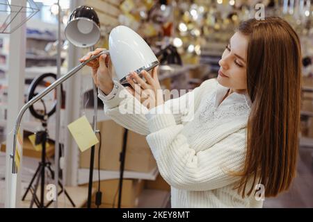 Young woman choosing new lamp to buy at furnishings lighting store. Stock Photo
