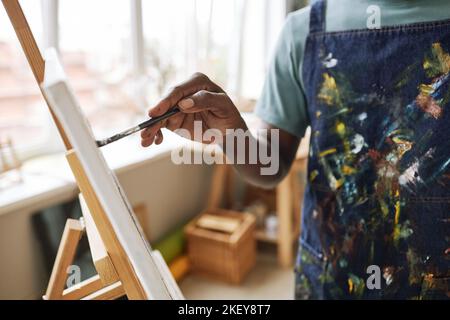 Hand of young contemporary painter with paintbrush creating new masterpiece on canvas while standing in front of easel Stock Photo