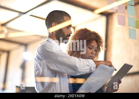 Entrepreneurs doing what they do best. two young professionals brainstorming with sticky notes on a glass wall in an office. Stock Photo