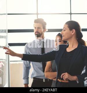 Shes got plans for this company. young businesspeople discussing ideas on a whiteboard during a meeting in an office. Stock Photo