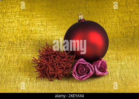 Christmas decocration with a red christmas bauble and two pink felt roses isolated on a golden background with texture. Stock Photo