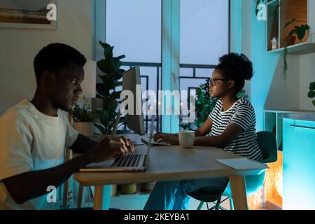 Professional focused African American man and woman doing programming sits at table in home office. Stock Photo