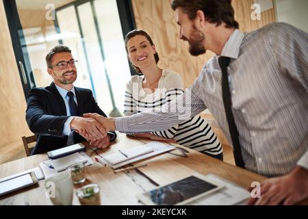Making deals. two businesspeople shaking hands in an office while a colleague look on. Stock Photo