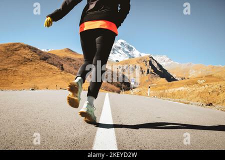 Back view woman close up on road run with comfortable hiking universal shoes with gummy pad on road with scenic mountains background. Kazbegi national Stock Photo