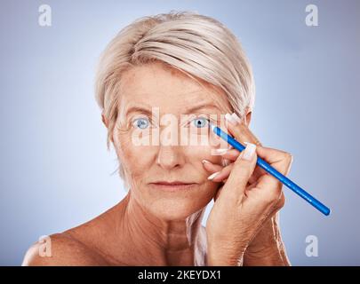 Beauty, makeup and mature woman with eyeliner pencil for blue eyes on studio background. Health, cosmetics and skincare, a portrait of beautiful Stock Photo