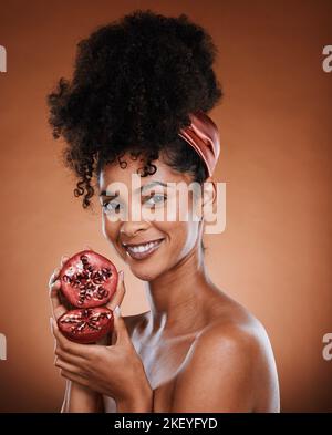 Face, beauty and pomegranate with a black woman model in studio on a brown background for natural vitamins. Skincare, wellness and luxury with an Stock Photo