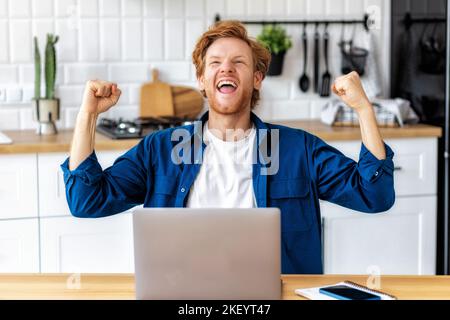 Portrait of excited young caucasian man celebrating success Young man reading good news using laptop Stock Photo