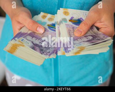 Woman counting money is holding a large amount of 20 British pound notes in cash Stock Photo