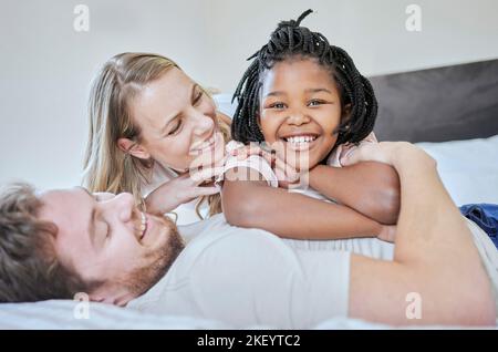 Love, adoption and family portrait, relax and smile on bed in home, happy and support with care. Mother, father and black girl, happiness and freedom Stock Photo